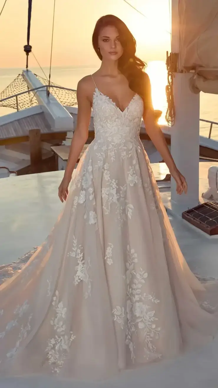 A woman wearing an elegant wedding gown with intricate floral patterns, standing on a boat at sunset.