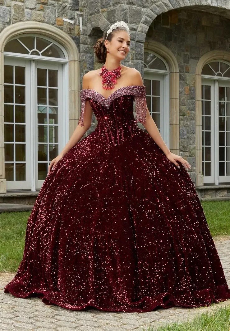 Young woman in a sparkling burgundy ballgown and tiara, standing outdoors and smiling.Young woman in a sparkling burgundy ballgown and tiara, standing outdoors and smiling.