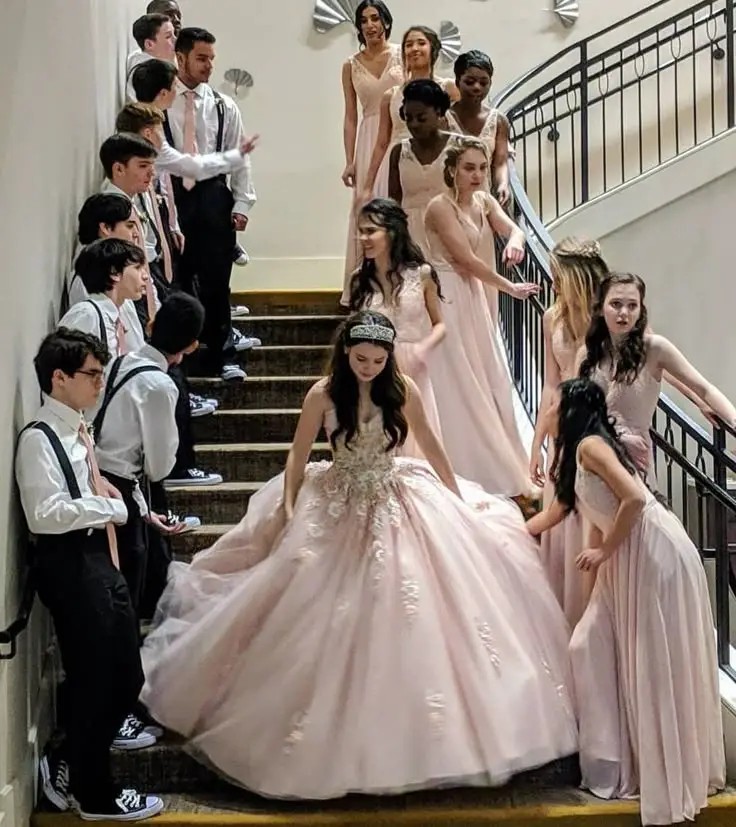 Quinceañera girl in a pink gown on a staircase, surrounded by her court.