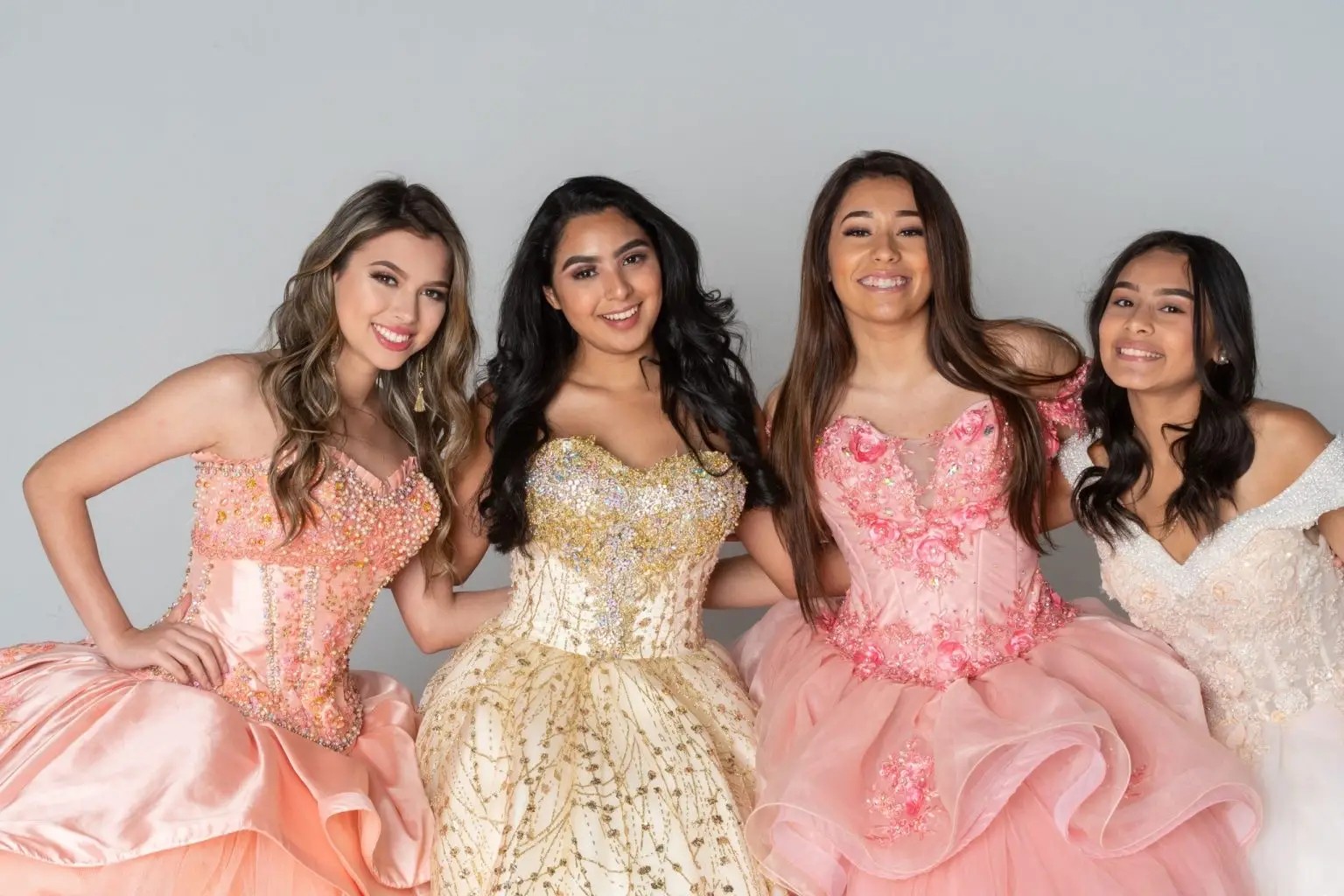 Four young women in colorful ballgowns smiling together.